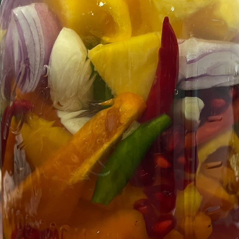 Colorful mixed peppers in a glass veseel visible red onions, and fruit pieces
